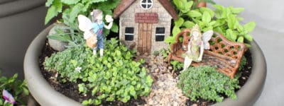 Brown fairy house with 2 fairies, herbs and pebble trail in grey pot