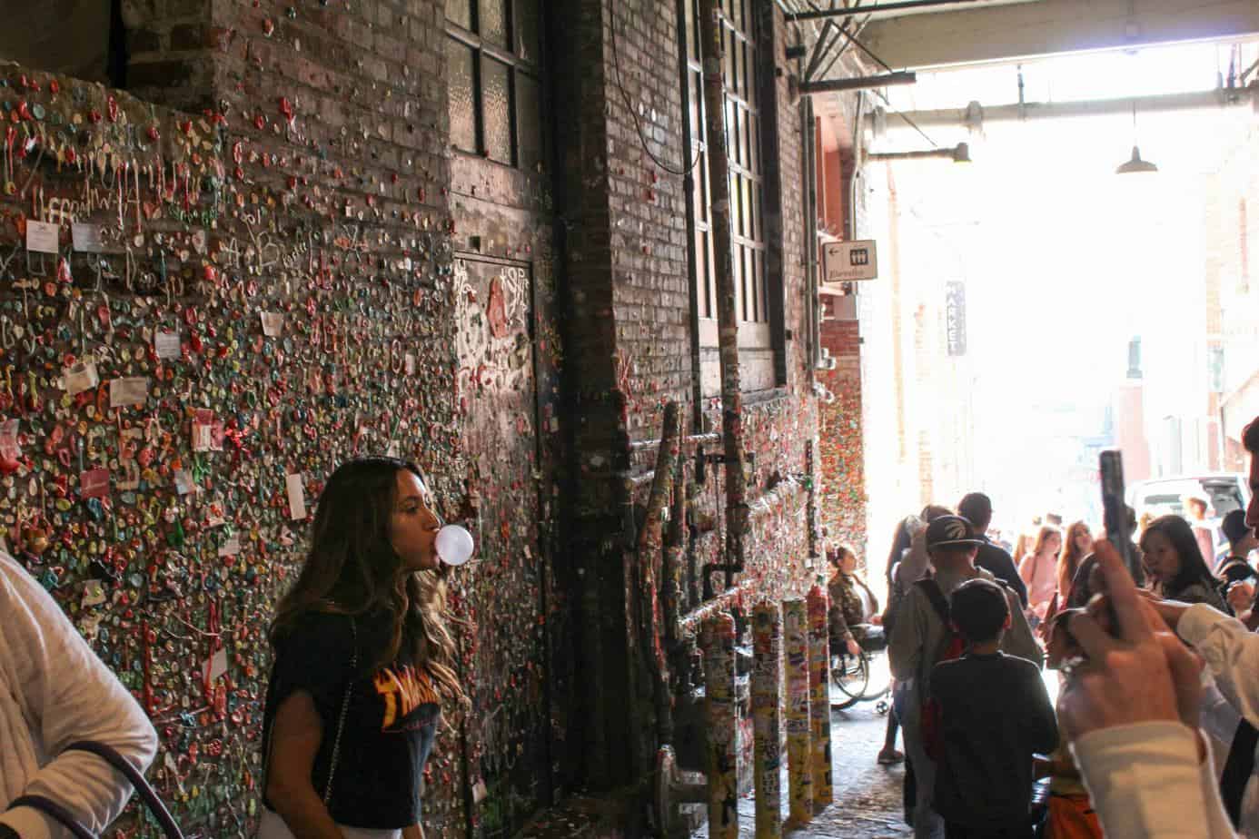 Girl blowing bubble in front of gum wall 