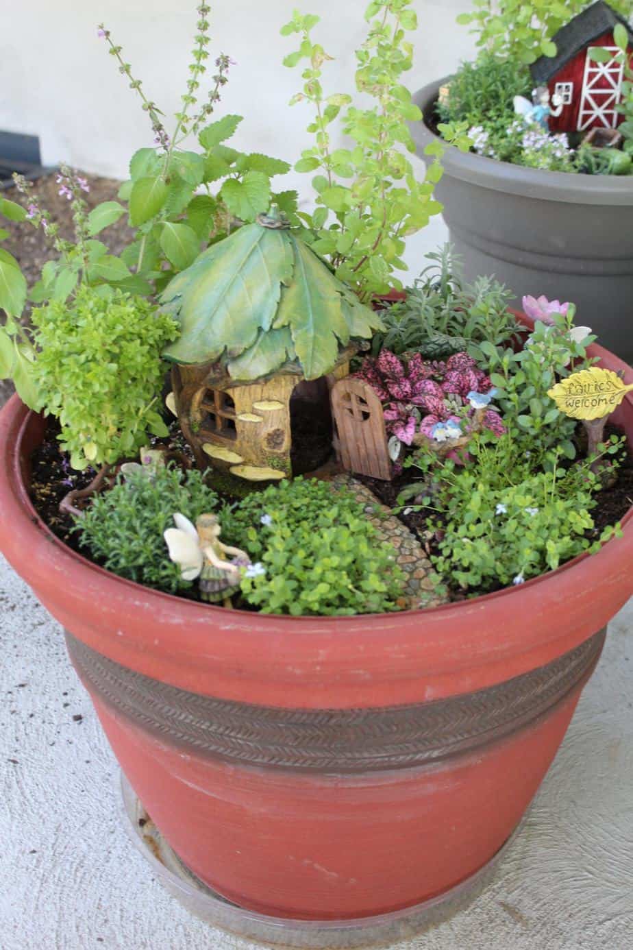 Close up of fairy garden with small house with a roof made of leaves and a fairy out front.