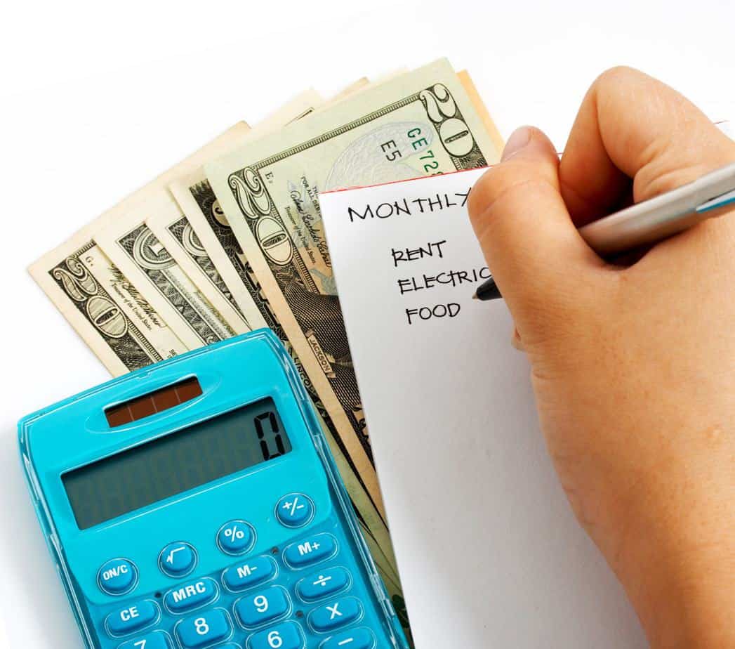 pad of paper with hand writing budget. calculator and money next to notebook