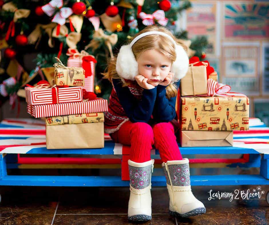 Young girl pouting with head in hands surrounded by Christmas tree and presents