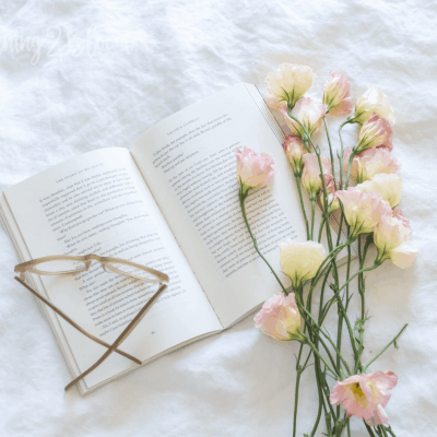 book, glasses and pink flowers laying on white background