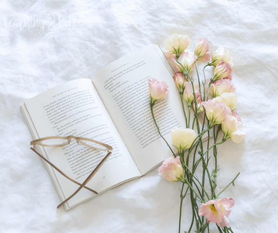 book, glasses and pink flowers laying on white background