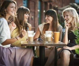 4 women sitting together outside at a coffee shop laughing